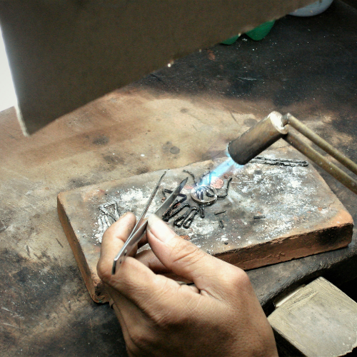 une main qui tient un chalumeau et qui soude un bijou